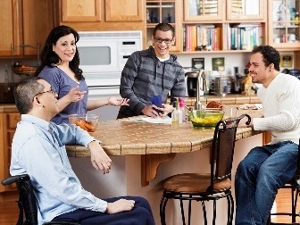 A group of people having a conversation in the kitchen in their home.