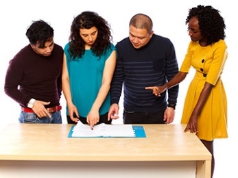 A group of four people looking at a document together on a table. 