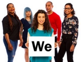 A group of people. A person at the front is holding a card that reads 'We'. 