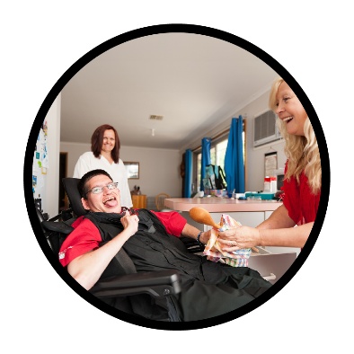 A person with disability smiling while being supported by 2 people in their home.