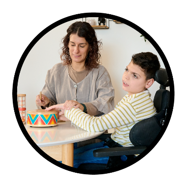 A person supporting a child. They are sitting at a table together.