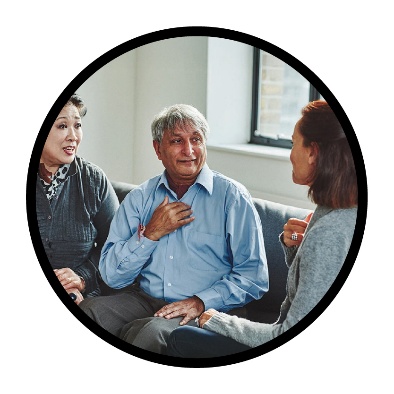 3 people sitting on a couch. 2 are pointing to themselves and talking.