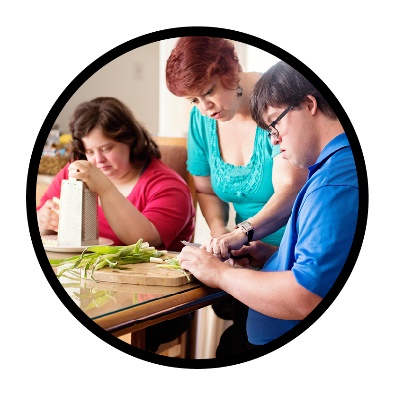 A person supporting 2 participants with cooking a meal. 