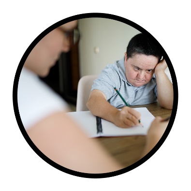 A Reference Group member writing on paper at a table next to a support worker. 