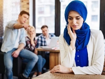 A woman wearing a head scarf looking upset as a group of people talk about her.