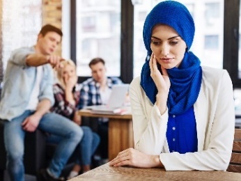 A woman wearing a head scarf looking upset as a group of people talk about her.