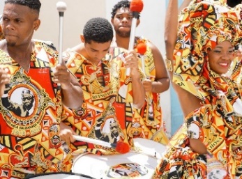 A group of people smiling and playing drums at a cultural celebration.