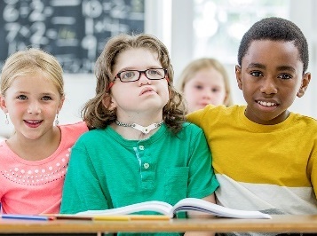 3 children smiling at school. One of them has a disability.