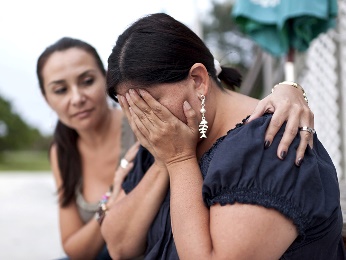 A woman crying into her hands, and another woman supporting her.