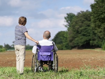 A person supporting a man in a wheelchair in a rural area.