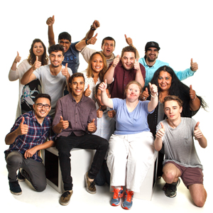 A group of diverse people sitting and standing together, all giving two thumbs up.