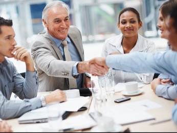 A group of people in a meeting. Two people are shaking hands across the table.