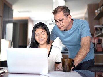 A male parent helping a young person use a laptop.