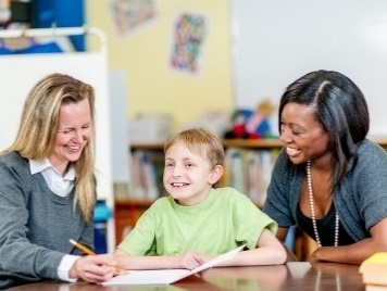 2 teachers supporting a young child in a classroom.