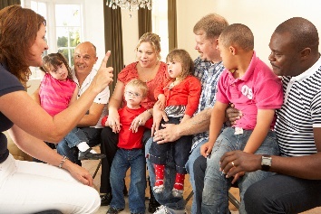 A group of people listening to someone speak. There are children and families in the audience. 