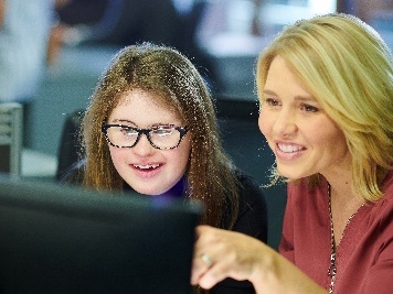 A person working with a young person with disability on a computer. 