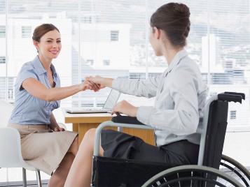 A person shaking hands with someone in a wheelchair. They are in an office. 