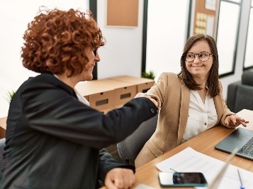 A person with intellectual disability shaking hands with a worker in an office.