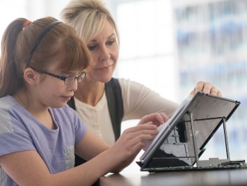 A worker supporting a child to use a tablet.