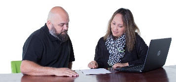 2 people sitting at a desk and looking at a document.
