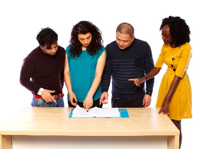 A group of people pointing to a document on a desk. They are having a conversation.