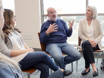 A group of people, sitting on chairs in a circle having a discussion