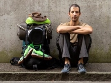 A person sitting in a gutter next to a large bag.